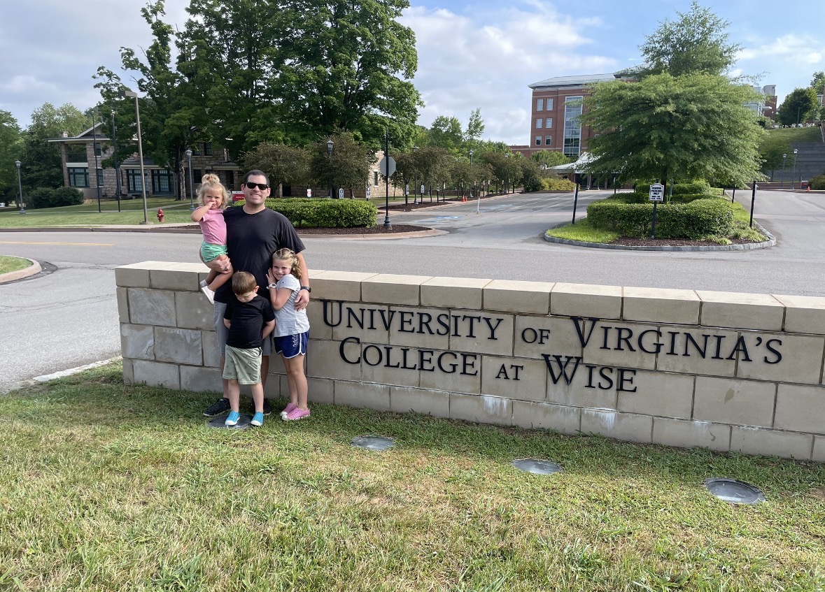 Christian smiling at entrance of college with his children 