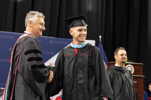 Student shaking hands after receiving graduate regalia.
