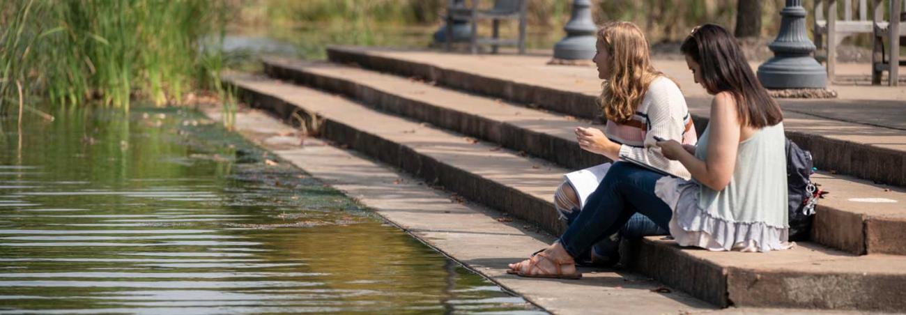 Students sitting on steps by the lake