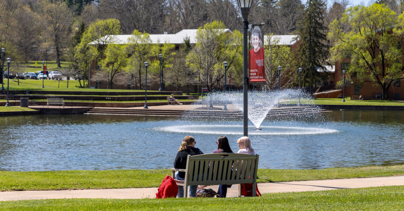 Students sitting on bench beside lake