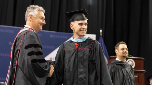 Student shaking hands after receiving graduate regalia.